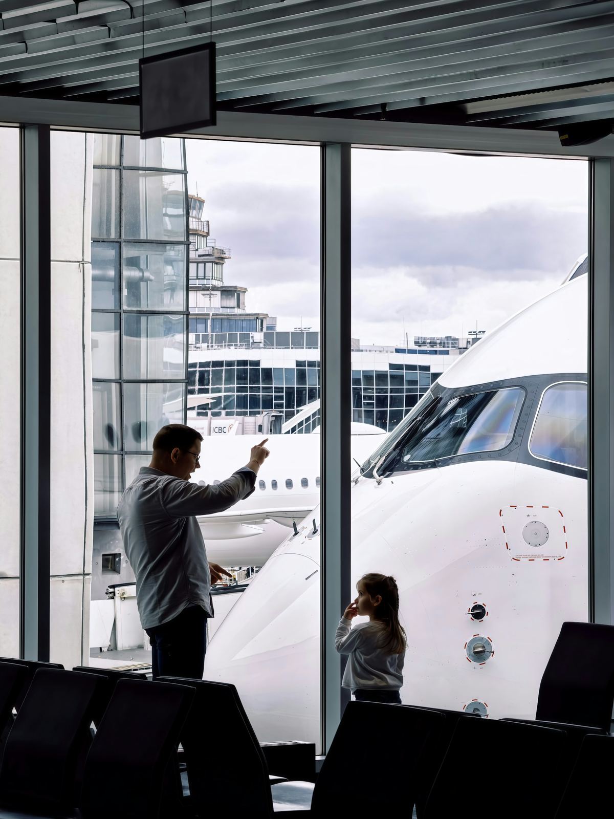 Un padre y su hija miran un avión en la puerta de embarque